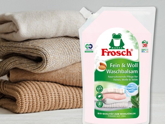 A Frosch Delicate almond detergent pouch stands between a basket and stacked towels